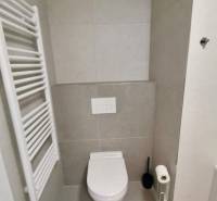 Fürdőszoba WC-vel és radiátorral egy egyszobás lakásban. Minimalista dizájn szürke csempével.