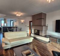 Tágas nappali kandallóval egy családi házban, világos bútorokkal, fa mintázatú padlóval.