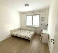 Hálószoba világos fallal, ággyal és íróasztallal, fa dekorációjú padlóval.