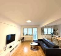 Nappali egy négyszobás lakásban, fa mintázatú padlóval és fekete kanapéval.