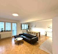 Nappali egy 4 szobás lakásban, fa dekoros padlóval és fekete kanapéval.