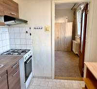 Konyha fehér csempékkel, tűzhellyel, szekrényekkel és kilátással az előszobára egy egyszobás lakásban.