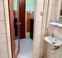 Fürdőszoba egy egyszobás lakásban tükörrel, mosdóval és fehér csempékkel.