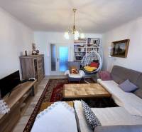 Nappali egy háromszobás lakásban fa mintázatú padlóval és könyvespolcokkal.