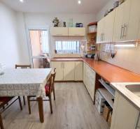 Konyha egy háromszobás lakásban fehér bútorokkal és fa dekorációjú padlóval.