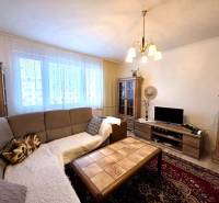 Nappali egy háromszobás lakásban kanapéval, csillárral, fa mintázatú padlóval és szekrényekkel.