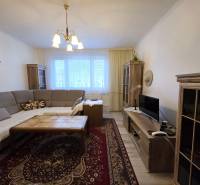 Nappali egy háromszobás lakásban sarokkanapéval és fa mintázatú padlóval.