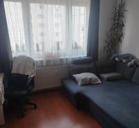 Garzonlakás kanapéval, íróasztallal és fa mintázatú padlóval.