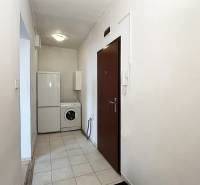 Az egyszobás lakás előszobája mosógéppel és hűtőszekrénnyel. Fehér falak, kerámia padló.