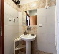 Fürdőszoba egy egyszobás lakásban mosdóval, tükörrel és fehér csempékkel.