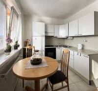 Konyha egy egyszobás lakásban ablakokkal, asztallal és növényekkel a párkányon.