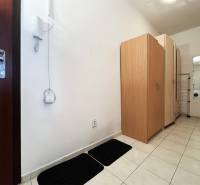 Folyosó egy egyszobás lakásban fehér falakkal, csempével és szekrényekkel.