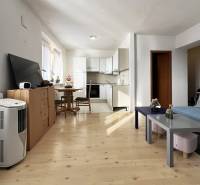 Nappali rész egy egyszobás lakásban konyhasarokkal és fa mintázatú padlóval.