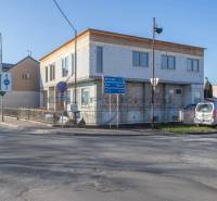 Épület Nagyléváron, az út mellett, parkoló autóval és közlekedési táblákkal.