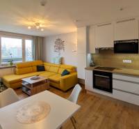 Nappali egy háromszobás lakásban kanapéval, karácsonyfával és konyhasorral.