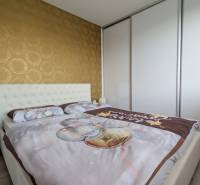 Hálószoba egy háromszobás lakásban tapétával és beépített szekrénnyel, fa dekorációjú padlóval.