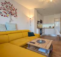 Világos konyha fa dekor padlóval és sárga kanapéval egy háromszobás lakásban.