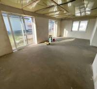 Tágas szoba egy családi házban nyers betonpadlóval, nagy ablakok biztosítják a bőséges fényt.