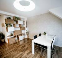 Étkezőasztal, székek és polcok dekorációs elemekkel egy háromszobás lakásban, fa dekoros padlóval.