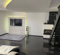 Nappali egy családi házban lépcsőházzal, kandallóval és falra szerelt televízióval.