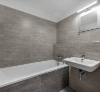 Fürdőszoba egy kétszobás lakásban káddal, mosdóval és szürke csempékkel.