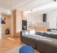 3 szobás lakás nappali része konyhával, szürke kanapéval és fa dekorációjú padlóval.