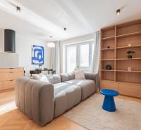 Világos nappali egy háromszobás lakásban kanapéval, fa dekorációval és kék kiegészítőkkel.