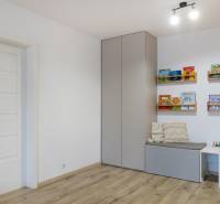 Gyerekszoba fa mintázatú padlóval, falra szerelt szekrénnyel és könyvespolcokkal.