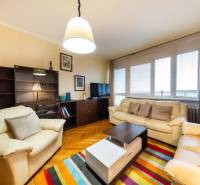 Nappali egy háromszobás lakásban kanapékkal, színes szőnyeggel és fa dekoros padlóval.