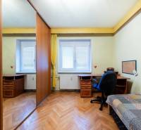 Szoba fa mintázatú padlóval, asztallal és szekrénnyel egy háromszobás lakásban.