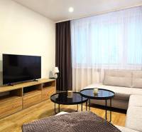 Nappali egy háromszobás lakásban kanapéval, televízióval és dohányzóasztallal, fa dekor padlón.