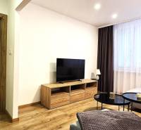 Nappali egy háromszobás lakásban fa dekoros padlóval és nagy televízióval.