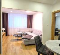 A háromszobás lakás nappalija kanapéval, asztallal és fa dekorációjú padlóval.