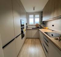 Konyha egy 4 szobás lakásban fa dekor padlóval, világos szekrényekkel, ablakkal.