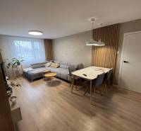 Nappali egy négy szobás lakásban, fa dekor padlóval, szürke kanapéval és étkezőasztallal.