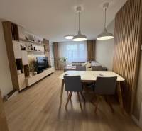 Nappali egy négy szobás lakásban kanapéval, TV-vel, étkezőasztallal és fa dekorációjú padlóval.