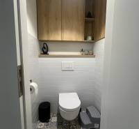 Fürdőszoba egy négyszobás lakásban színes csempével és falra szerelt fa szekrényekkel.