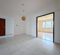 A csempézett folyosó egy világos nappaliba vezet, amelynek padlója fa dekorációval van ellátva.