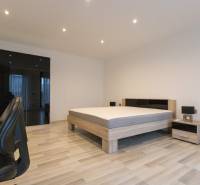 2 szobás lakás fa mintázatú padlóval, ággyal, szekrénnyel és irodai székkel.