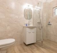 Fürdőszoba fa mintázatú padlóval, zuhanyzóval és szekrénnyel egy háromszobás lakásban.