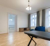 Nappali egy háromszobás lakásban, fa hatású padlóval és kék kanapéval.