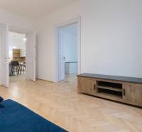 Háromszobás lakás nappalija kék kanapéval és fa dekorációjú padlóval.