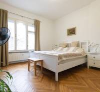 Hálószoba világos bútorokkal, nagy ablakkal és fa dekorációjú padlóval egy kétszobás lakásban.