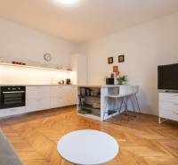 Nappali egy kétszobás lakásban konyhával, fa hatású padlóval, TV-vel és asztallal.