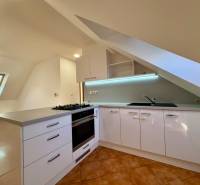 Világos konyha tetőtéri ablakkal, sarok munkalappal és kerámia padlóval egy kétszobás lakásban.