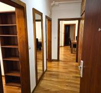 Folyosó fa dekor padlóval egy háromszobás lakásban, beépített szekrények és tükör.