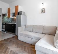 Nappali konyhasarokkal, sarokkanapéval és fa dekorációjú padlóval egy kétszobás lakásban.