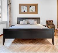 Világos szoba ággyal, székkel és fa dekorációjú padlóval egy kétszobás lakásban.