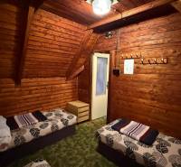 A faház belső tere fa burkolattal, ágyakkal és csillárral, otthonos környezet a pihenéshez.