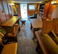 A kunyhó belseje faasztalokkal és padokkal, kilátás a kertre.